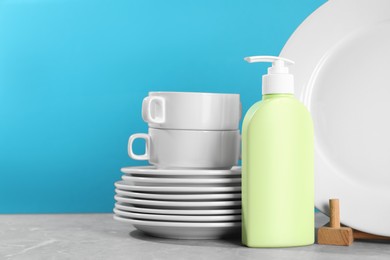 Set of clean tableware and dish detergent on grey table against light blue background. Space for text