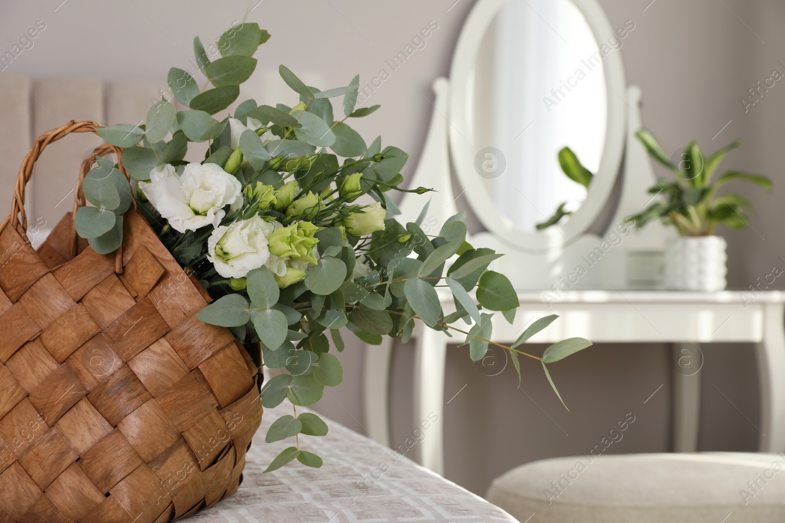 Photo of Stylish wicker basket with bouquet on bed indoors, space for text