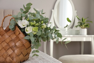 Stylish wicker basket with bouquet on bed indoors, space for text