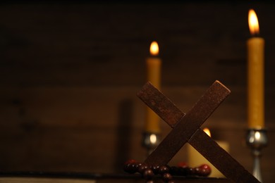 Photo of Wooden cross, rosary beads and church candles against blurred background, space for text