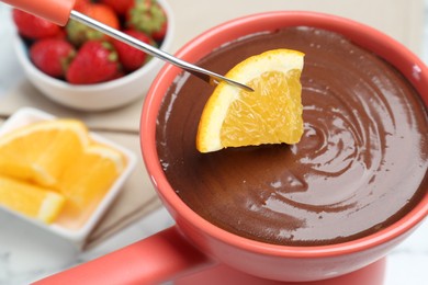 Dipping fresh orange into fondue pot with melted chocolate at table, closeup