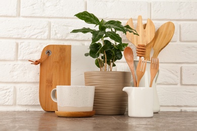 Photo of Potted plant and set of kitchenware on grey table near white brick wall. Modern interior design
