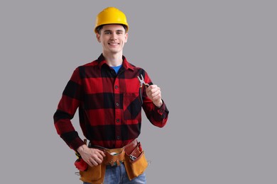 Young man holding pliers on grey background, space for text