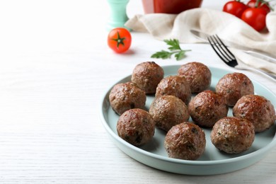 Photo of Tasty cooked meatballs served on white wooden table. Space for text