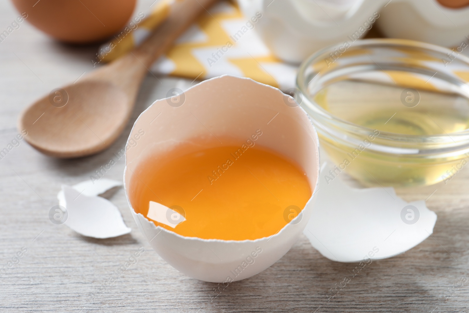 Photo of Cracked eggshell with raw yolk on white wooden table, closeup