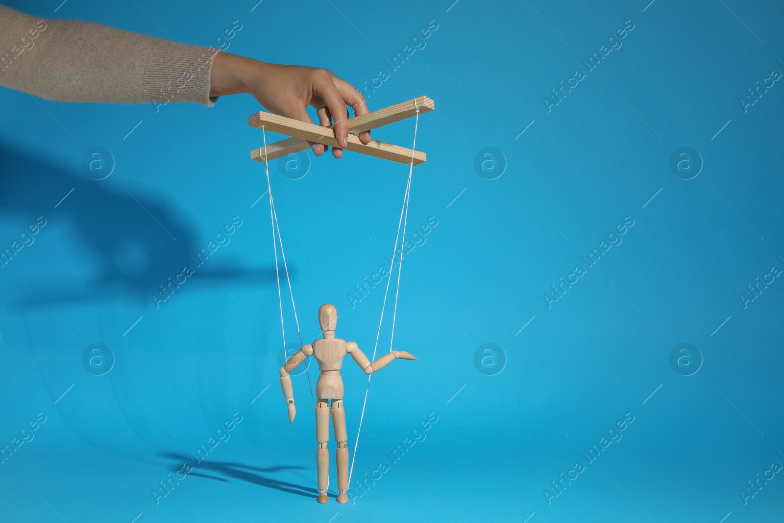 Photo of Woman pulling strings of puppet on light blue background, closeup