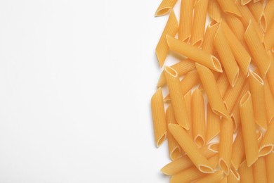 Photo of Raw penne pasta on white background, top view. Space for text