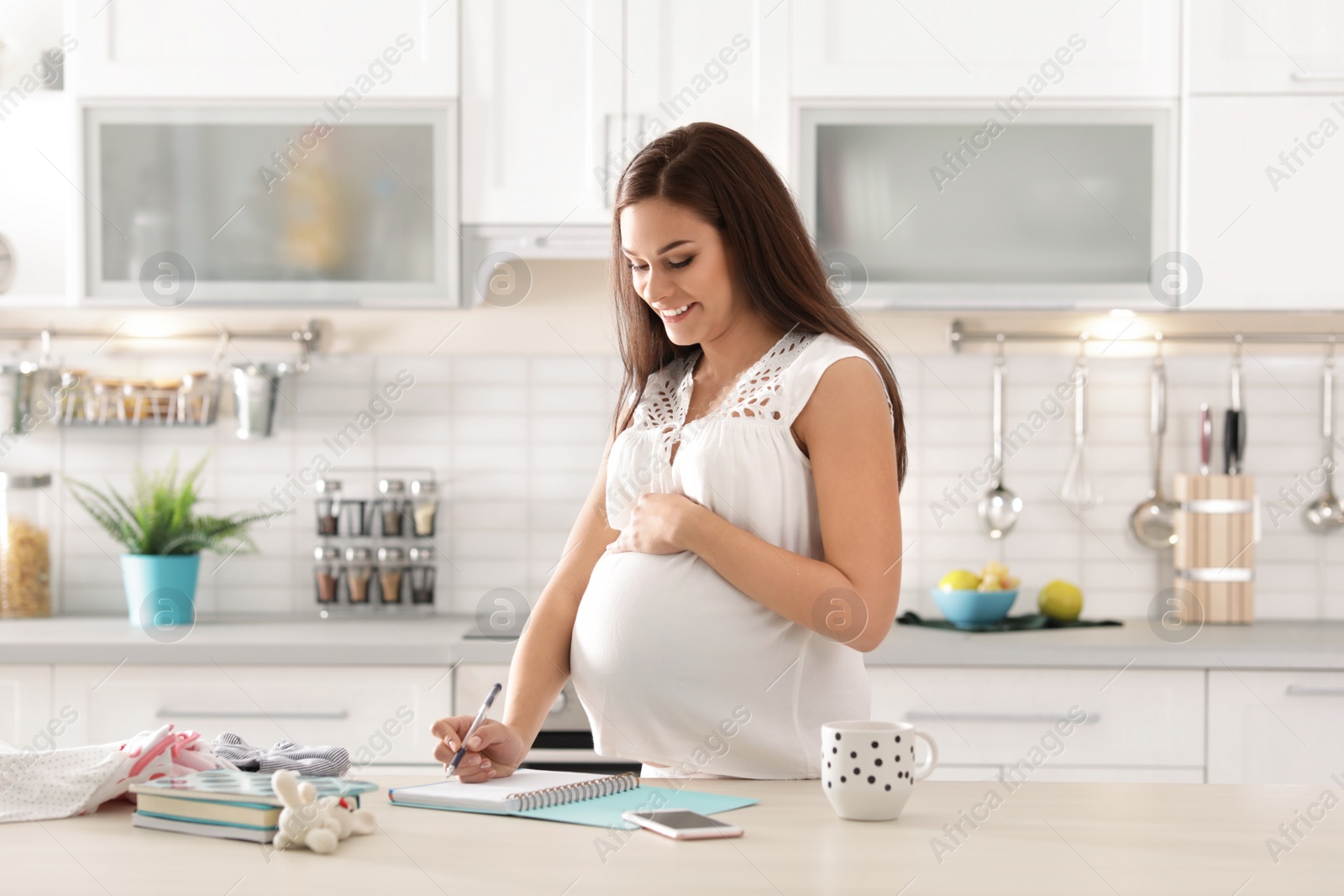 Photo of Pregnant woman writing packing list for maternity hospital in kitchen