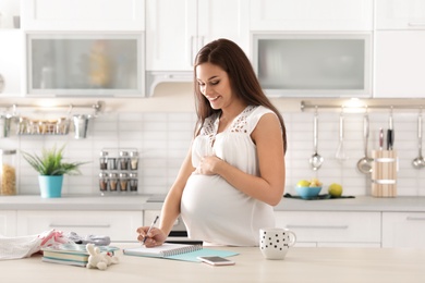 Pregnant woman writing packing list for maternity hospital in kitchen