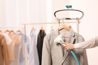 Woman steaming jacket on hanger in room, closeup. Space for text