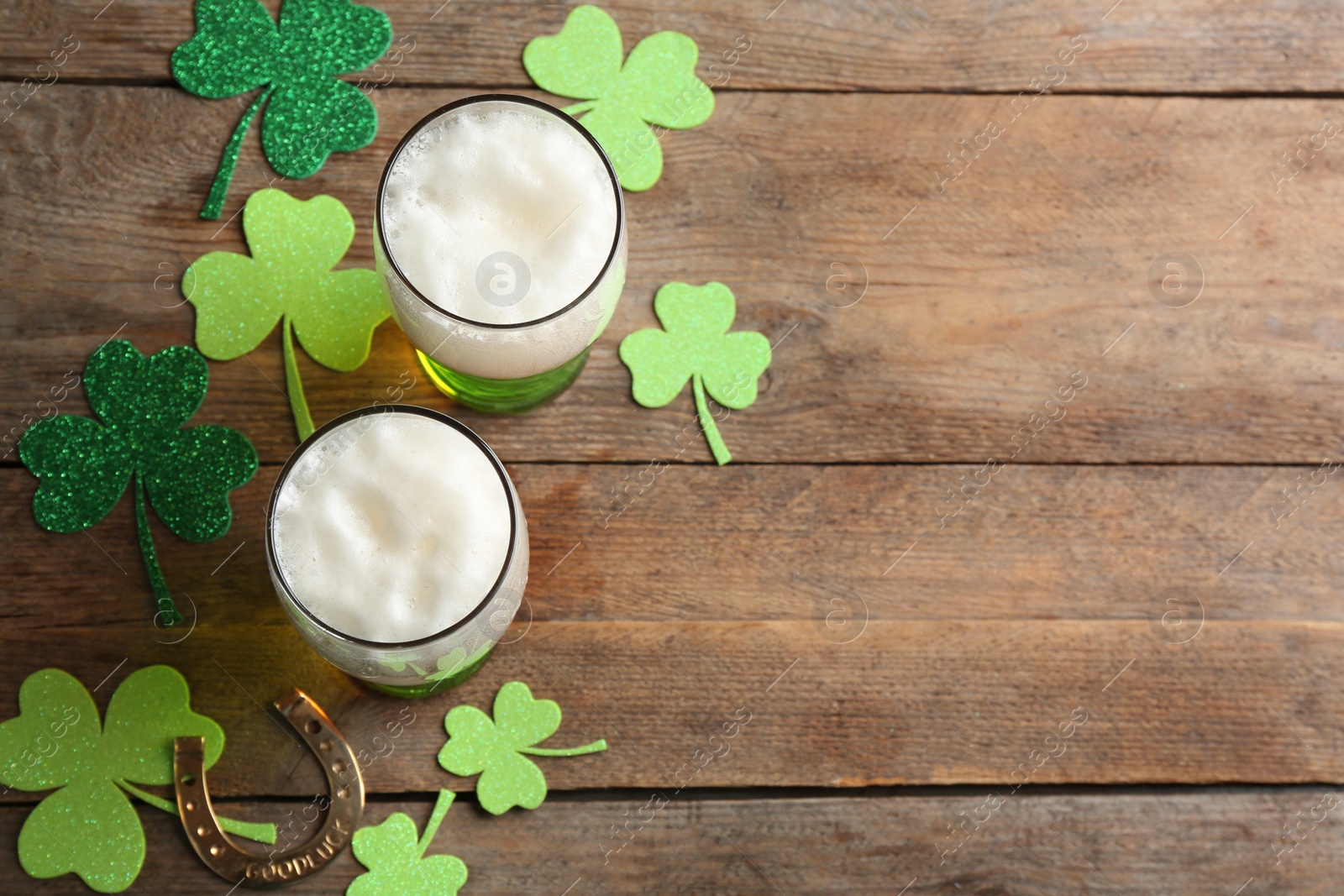 Photo of Green beer, horseshoe and clover leaves on wooden table, flat lay with space for text. St. Patrick's Day celebration