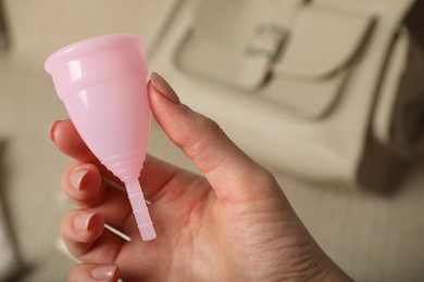 Photo of Woman holding pink menstrual cup on blurred background, closeup