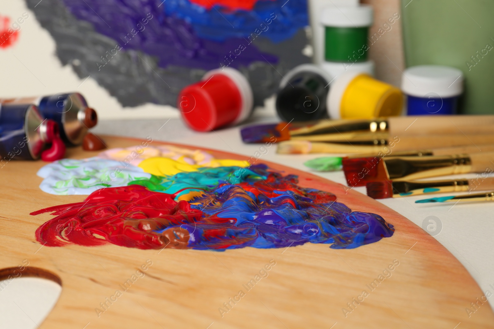 Photo of Artist's palette with mixed paints and brushes on table, closeup