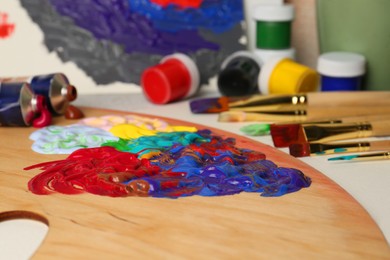 Artist's palette with mixed paints and brushes on table, closeup