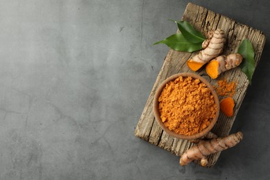 Photo of Aromatic turmeric powder and raw roots on grey table, top view. Space for text