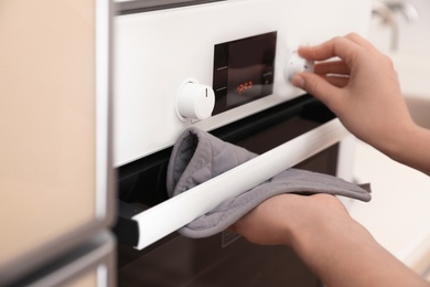 Photo of Woman adjusting electric oven in kitchen, closeup