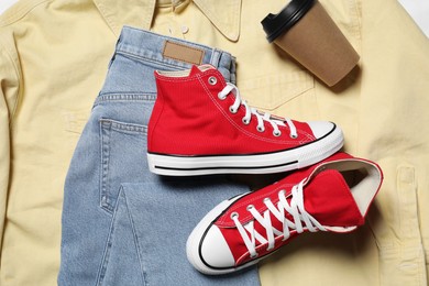 Photo of Pair of stylish red shoes, jeans and paper cup on yellow shirt, flat lay