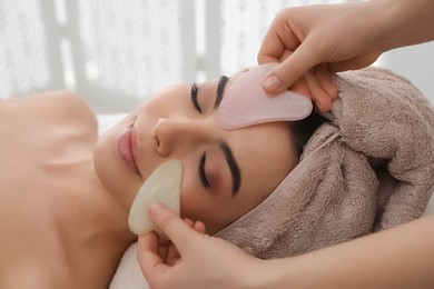 Photo of Young woman receiving facial massage with gua sha tools in beauty salon