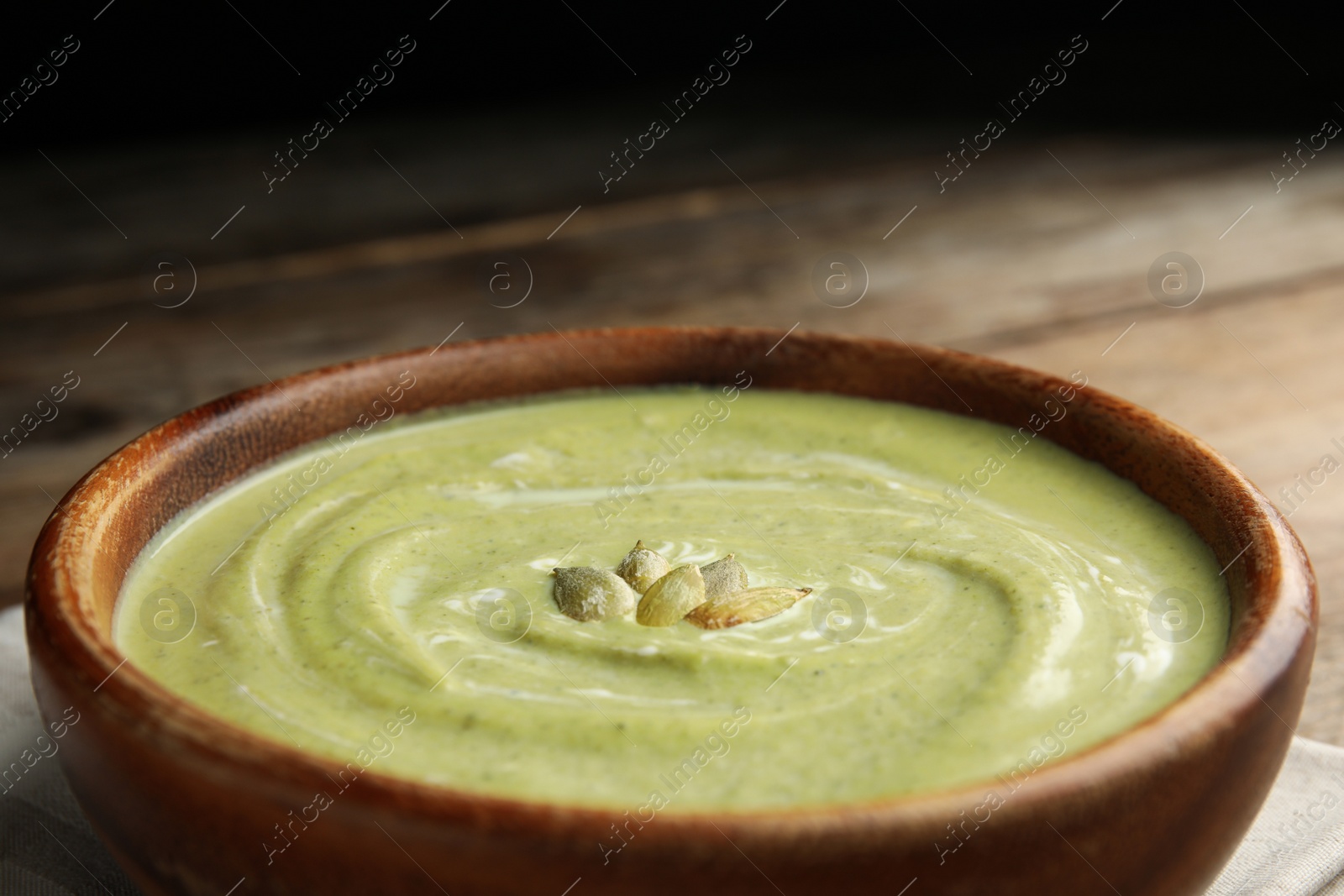 Photo of Bowl of delicious broccoli cream soup with pumpkin seeds, closeup