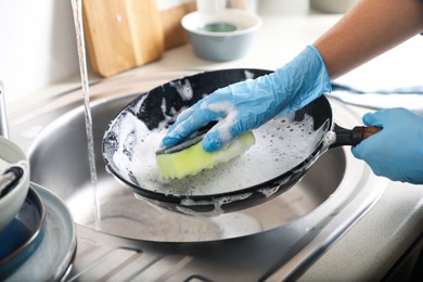 Photo of Woman washing dirty frying pan in sink indoors, closeup