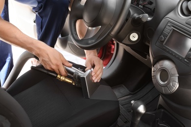 Photo of Male worker removing dirt from car seat with professional vacuum cleaner