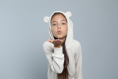 Photo of Cute girl in adorable white pajamas blowing kiss on light grey background