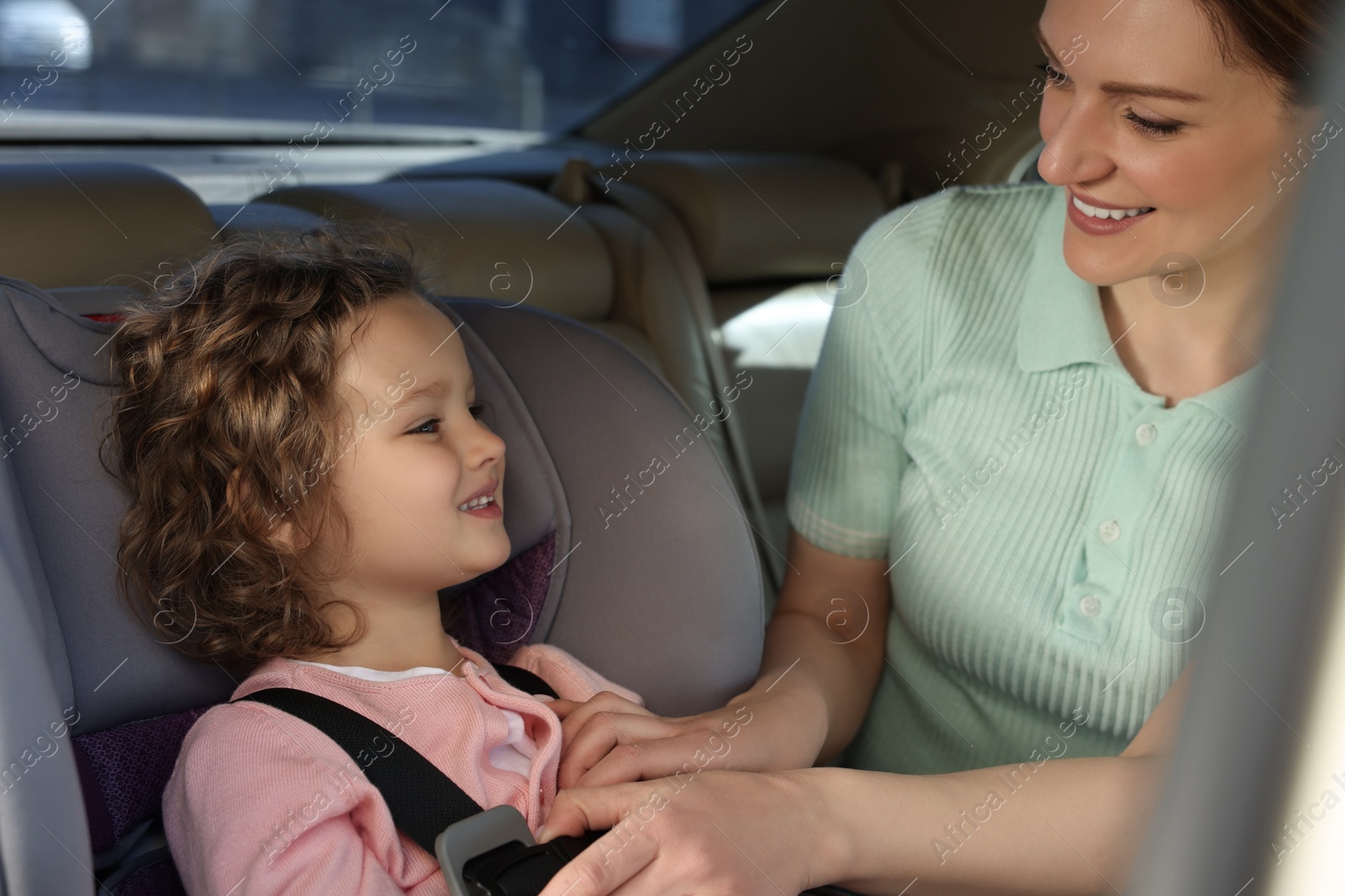 Photo of Mother fastening her daughter in child safety seat inside car