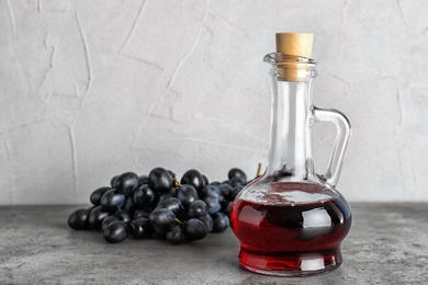 Photo of Glass jug with wine vinegar and fresh grapes on gray table