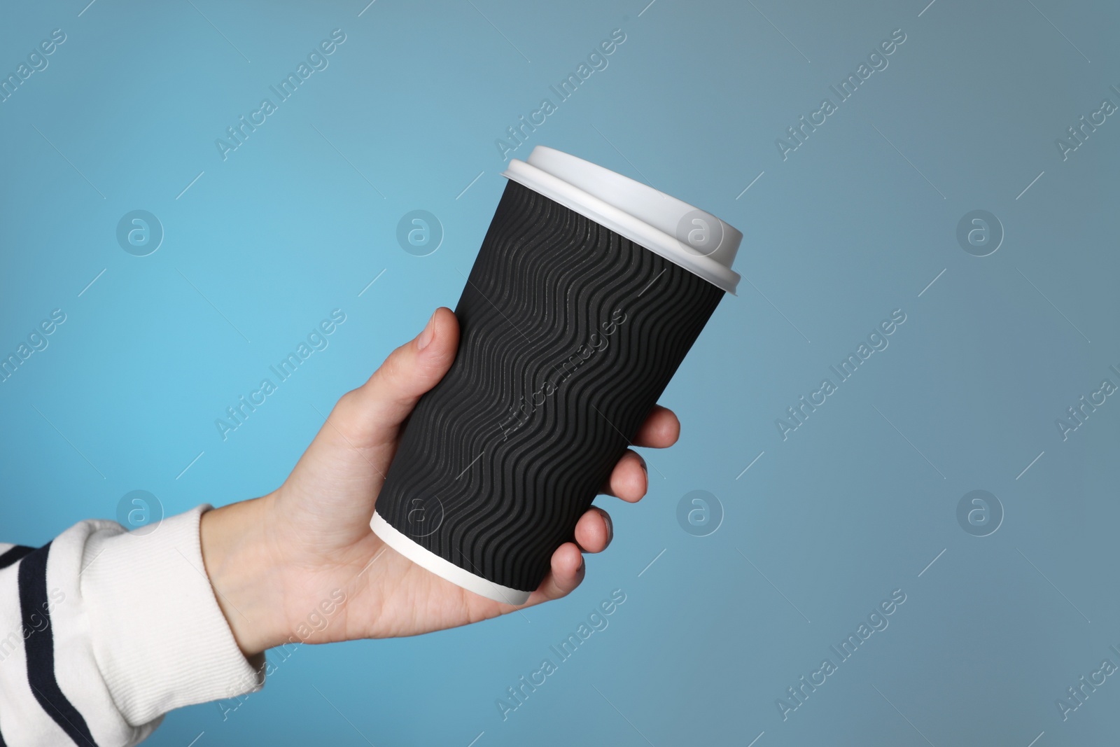 Photo of Woman holding takeaway paper coffee cup on blue background, closeup