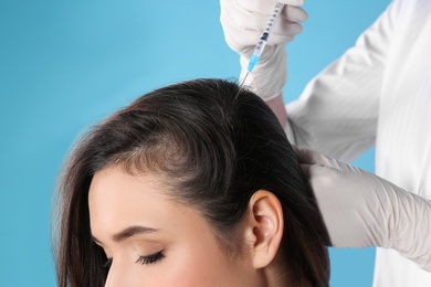 Young woman with hair loss problem receiving injection on color background, closeup