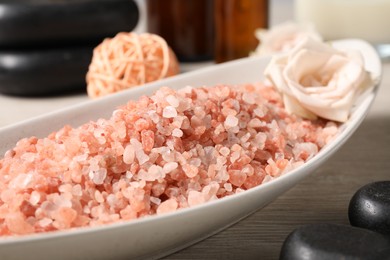 Photo of Natural sea salt in bowl, spa stones, rose and rattan ball on wooden table, closeup