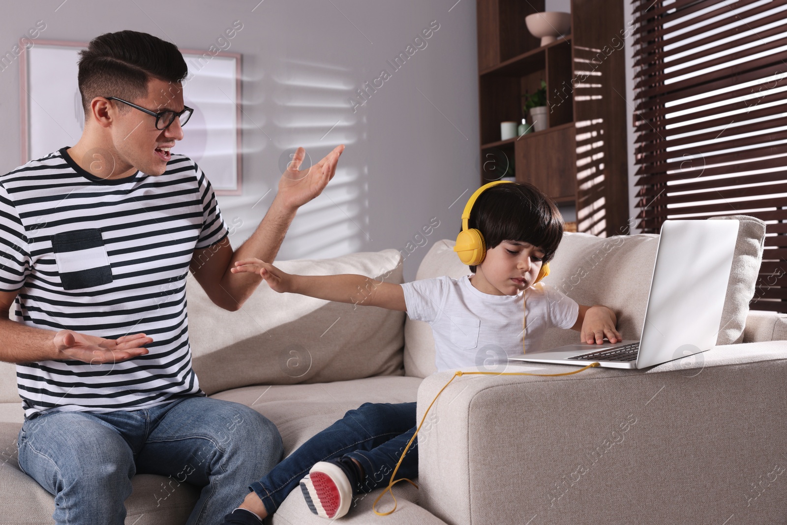 Photo of Internet addiction. Man scolding his son while he using laptop in living room