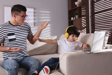 Internet addiction. Man scolding his son while he using laptop in living room