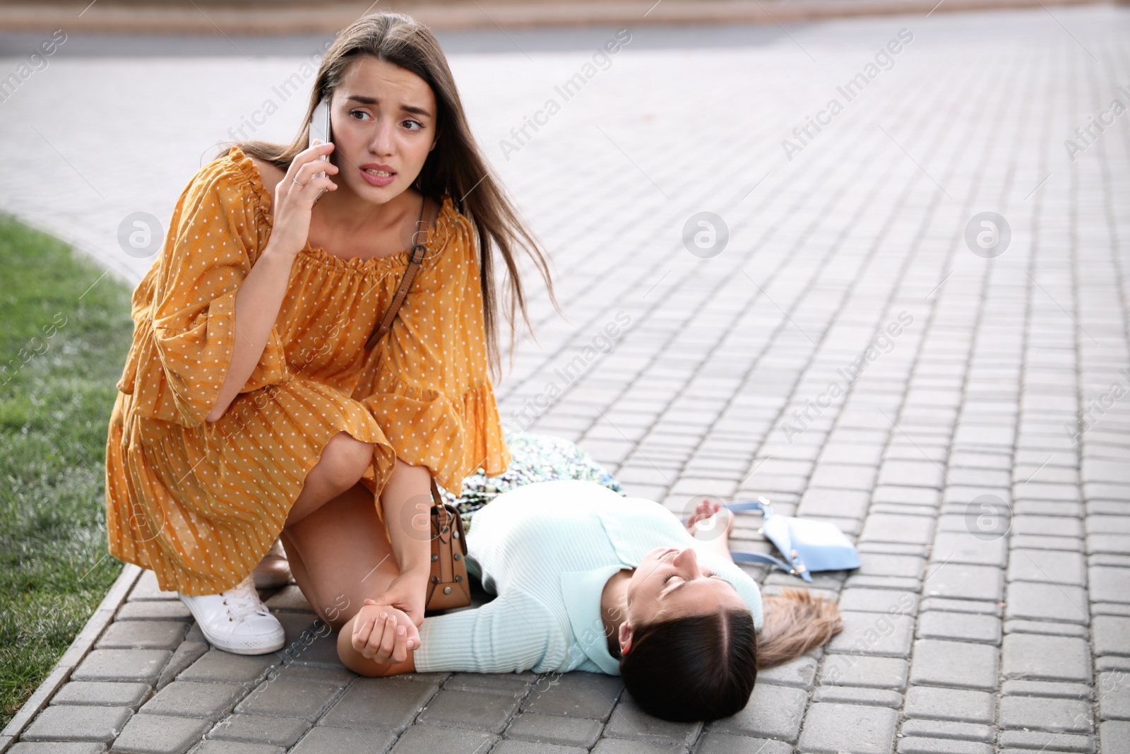 Photo of Woman calling ambulance to help unconscious person with heart attack on city street