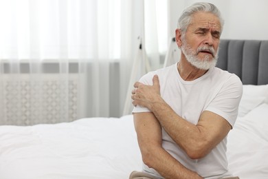 Arthritis symptoms. Man suffering from pain in shoulder on bed at home, space for text