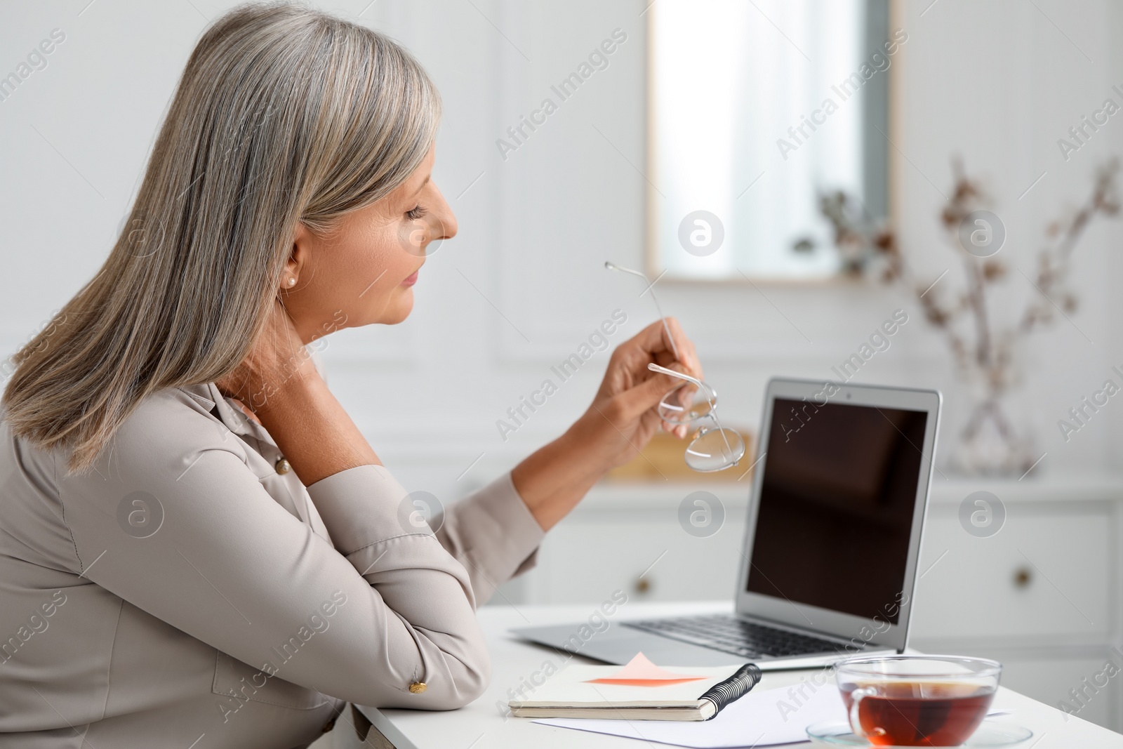 Photo of Woman suffering from neck pain at workplace in room