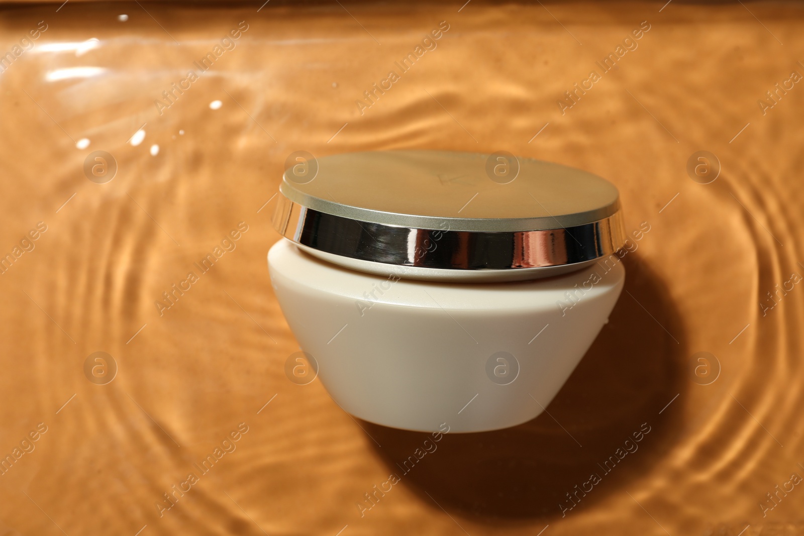 Photo of Jar of hair care cosmetic product in water on orange background, top view