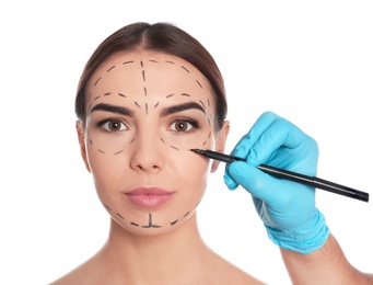 Doctor drawing marks on woman's face for cosmetic surgery operation against white background