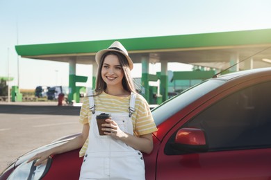 Beautiful young woman with coffee near car at gas station