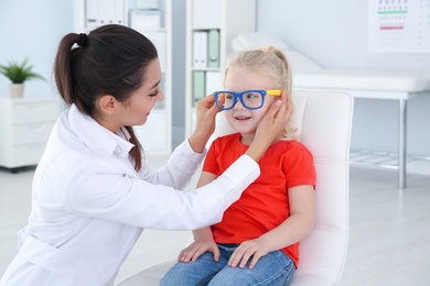 Photo of Children's doctor putting glasses on little girl in clinic