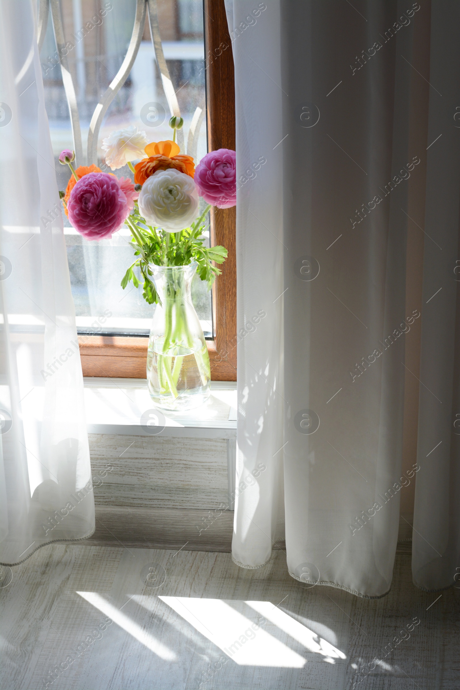 Photo of Bouquet of beautiful bright ranunculus flowers in glass vase indoors
