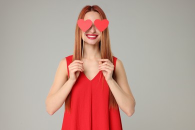 Photo of Young woman in red dress covering her eyes with paper hearts on light grey background