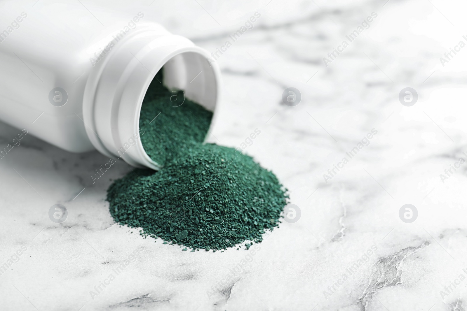 Photo of Bottle and spirulina algae powder on marble table, closeup. Space for text