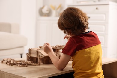 Photo of Little boy playing with wooden castle at table in room. Child's toy