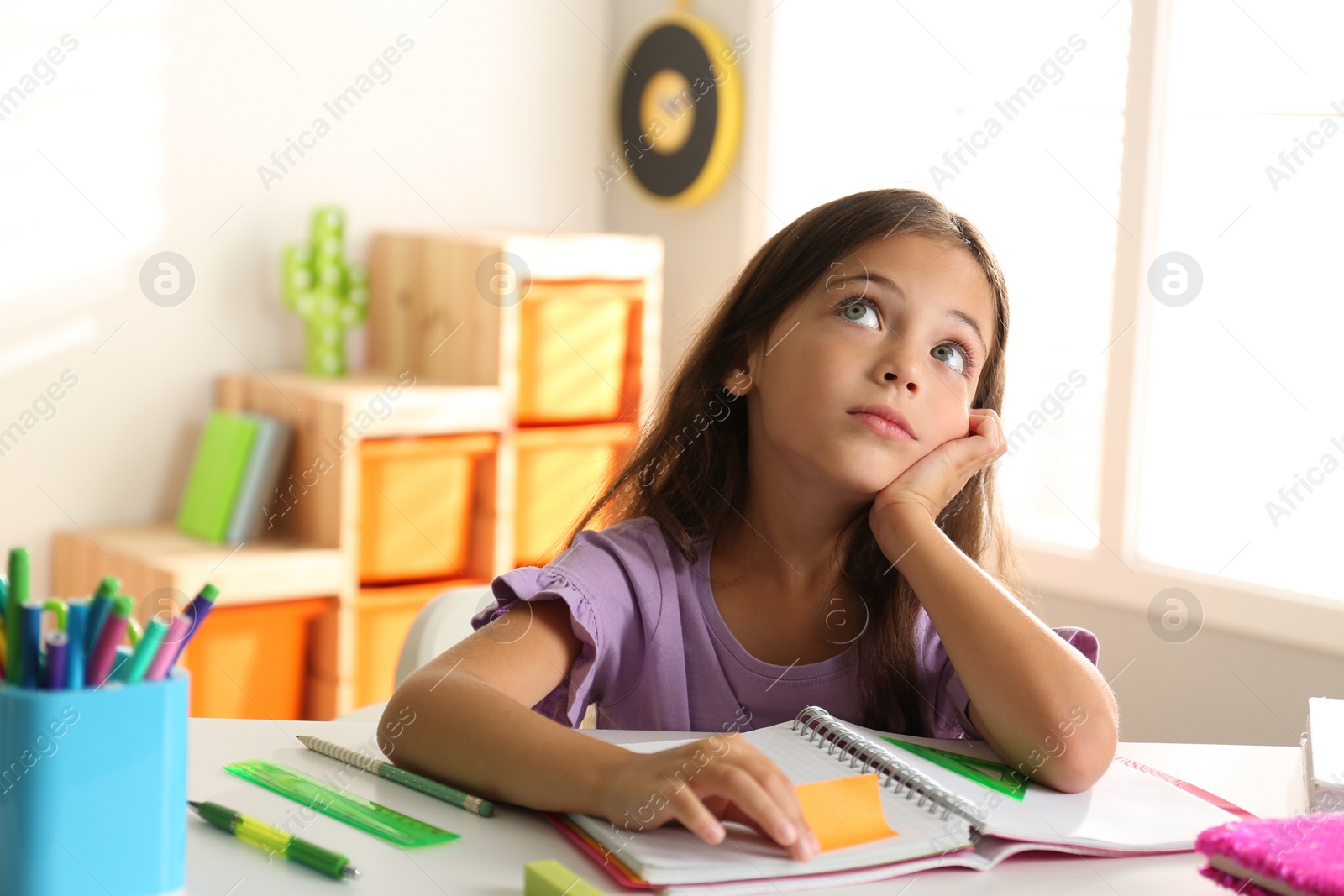 Photo of Little girl doing homework at table indoors