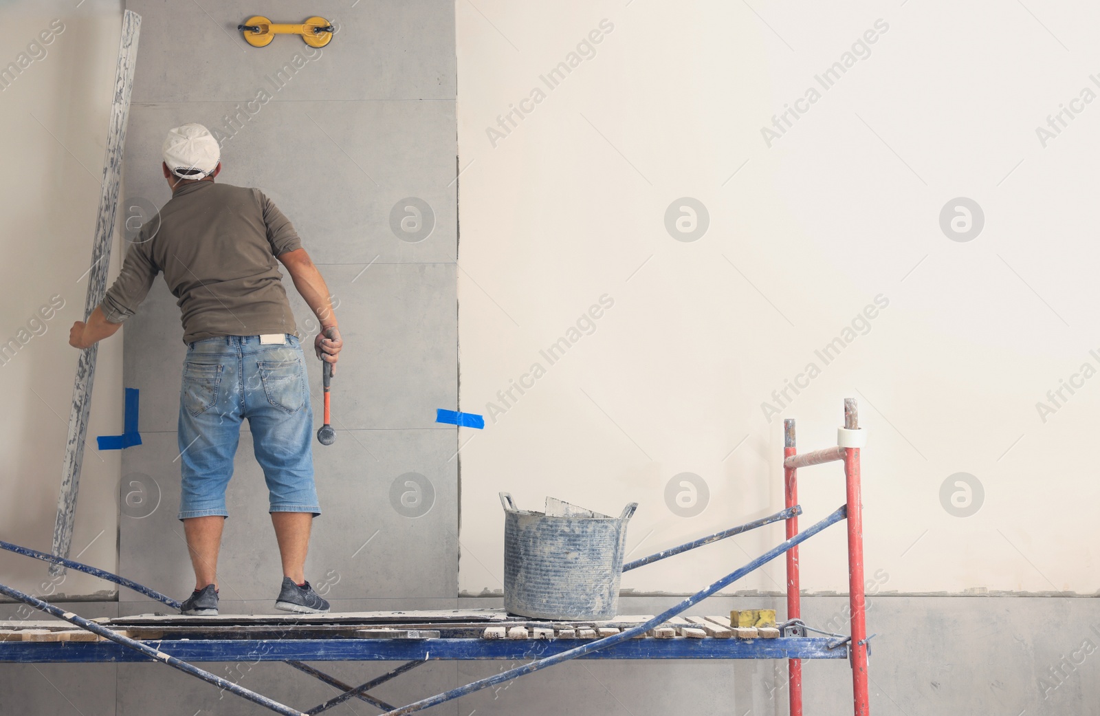 Photo of Worker installing tile on wall indoors, back view