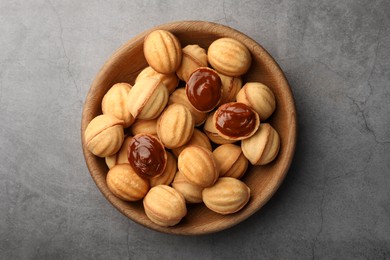 Photo of Delicious nut shaped cookies with boiled condensed milk in wooden bowl on gray textured table, top view
