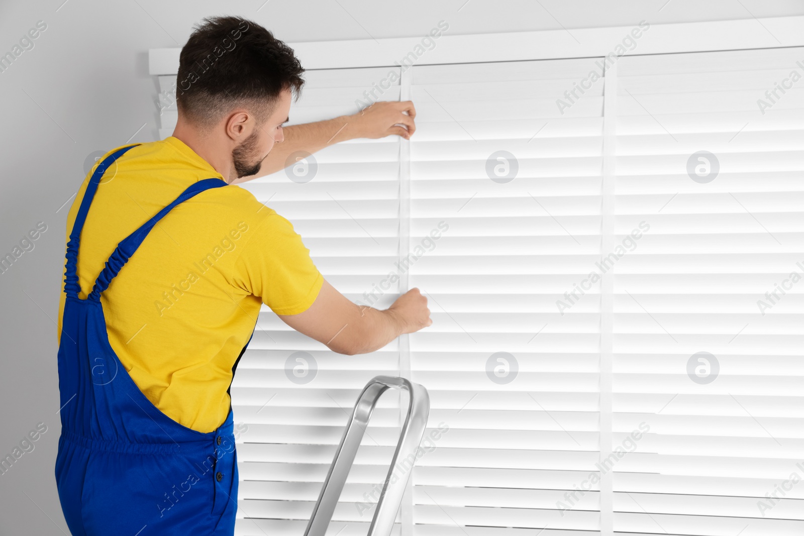 Photo of Worker in uniform installing horizontal window blinds indoors