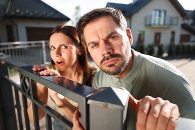Photo of Concept of private life. Curious couple spying on neighbours over fence outdoors
