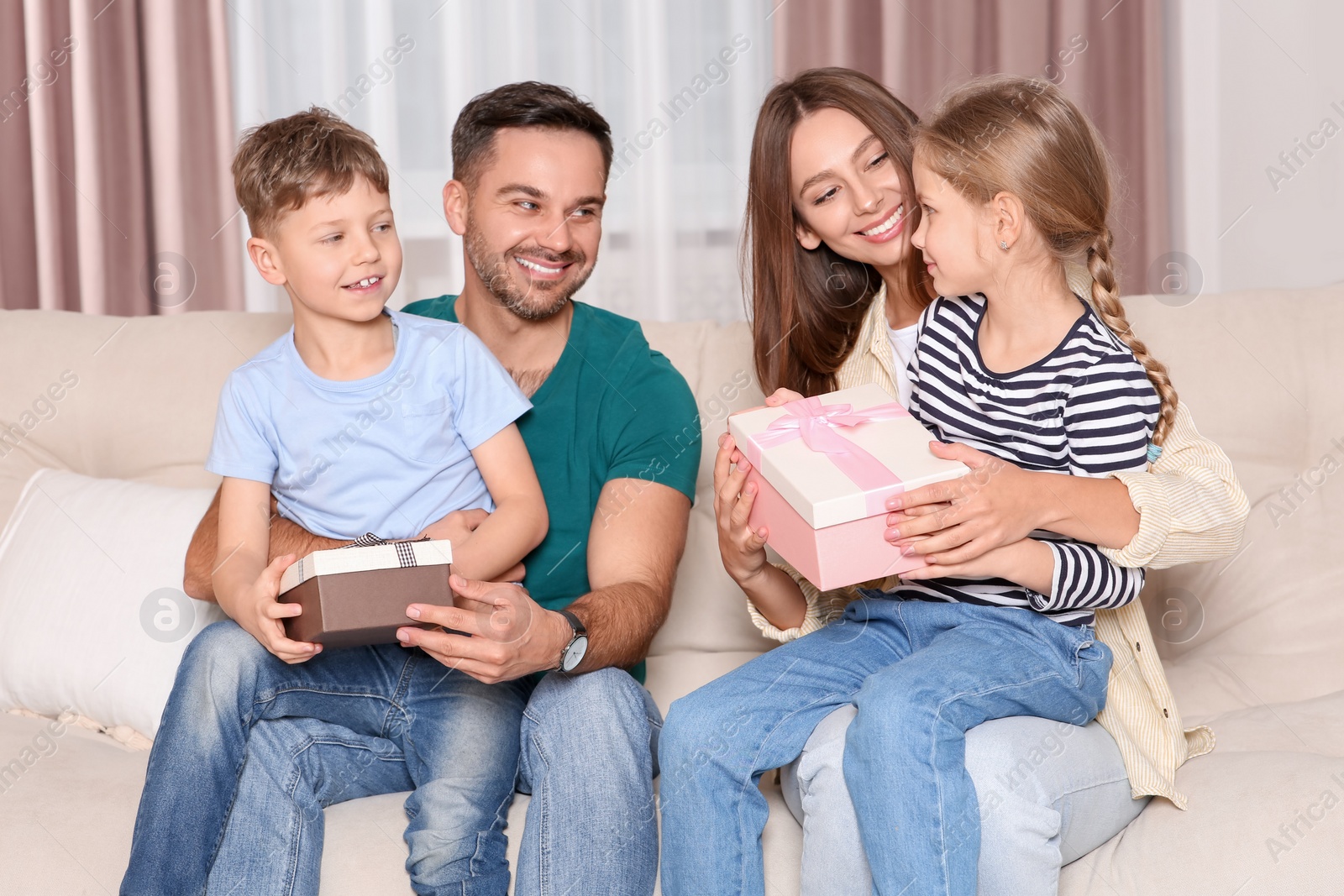 Photo of Happy family presenting each other with gifts on sofa at home